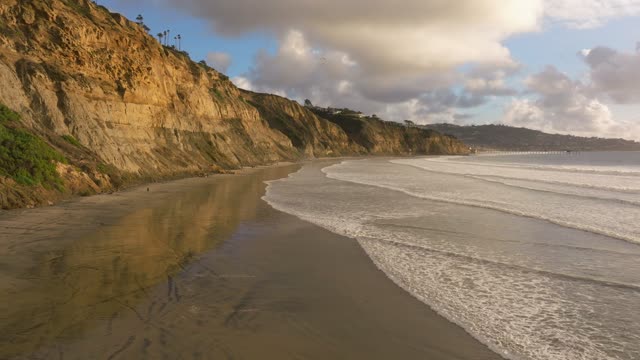 Low aerial view of the beach, the surf and the pier at Black’s Beach.