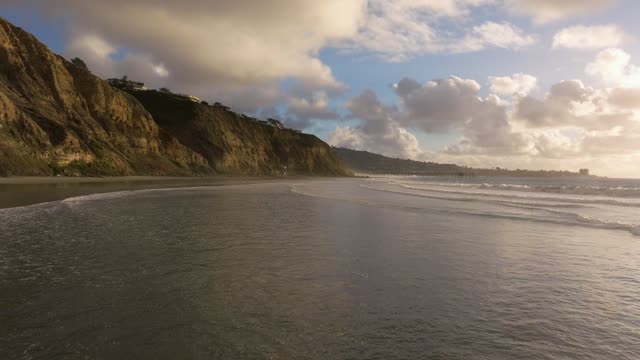 Low aerial view of the beach, the surf and the pier at Black’s Beach.