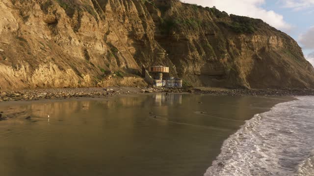 Low aerial view of the cliffs, the surf and the ocean at Black’s Beach, with people walking.