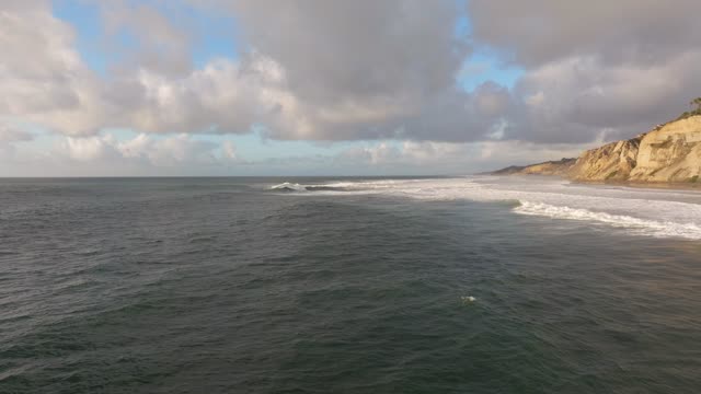 Low aerial view of the cliffs, the surf and the ocean at Black’s Beach.