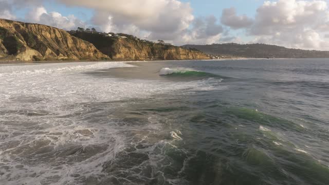 Low aerial view of the cliffs, the surf and the ocean at Black’s Beach.