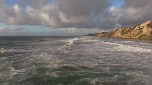 Low aerial view of the cliffs, the surf and the ocean at Black’s Beach.