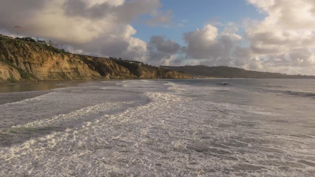 Low aerial view of the cliffs, the surf and the ocean at Black’s Beach.