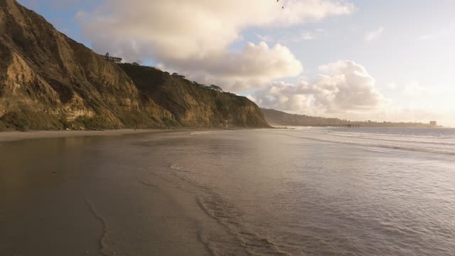 Low aerial view of the beach, the surf and the ocean at Black’s Beach, with people walking.