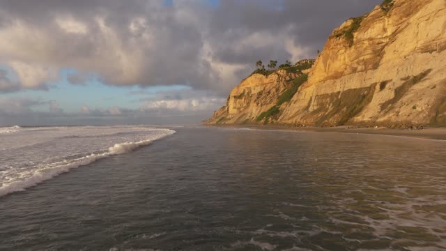 Low aerial view of the beach, the surf and the ocean at Black’s Beach, with people walking.