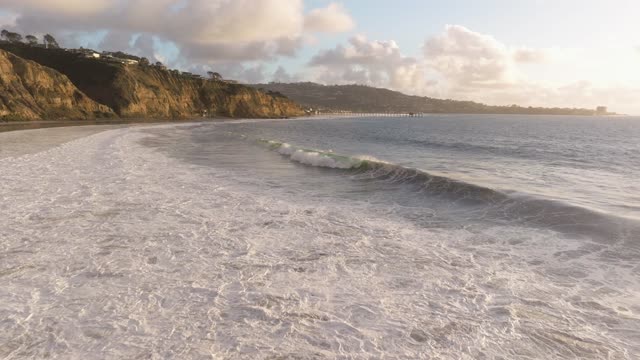 Low aerial view of the beach, the surf and the pier at Black’s Beach.