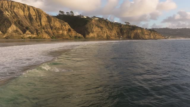 Low aerial view of the cliffs, the surf and the ocean at Black’s Beach.
