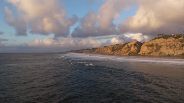 Low aerial view of the cliffs, the surf and the ocean at Black’s Beach.