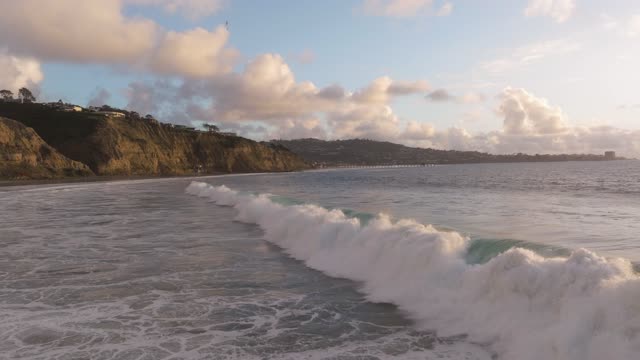 Low aerial view of the cliffs, the surf and the pier at Black’s Beach.