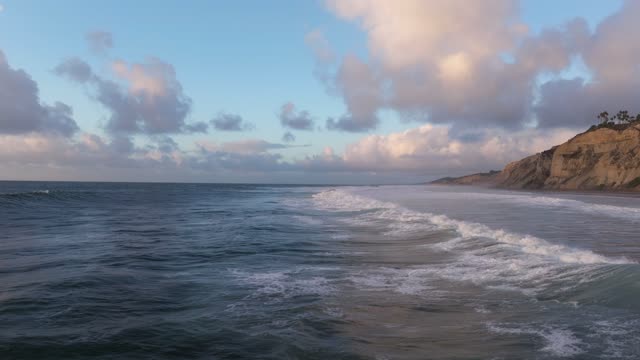 Low aerial view of the cliffs, the surf and the ocean at Black’s Beach.
