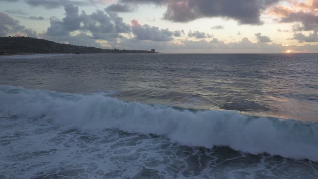 Low aerial view of the beach, the surf and the pier at Black’s Beach.