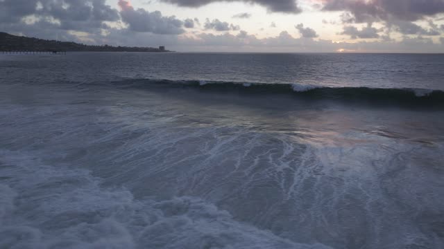 Low aerial view of the beach, the surf and the pier at Black’s Beach.
