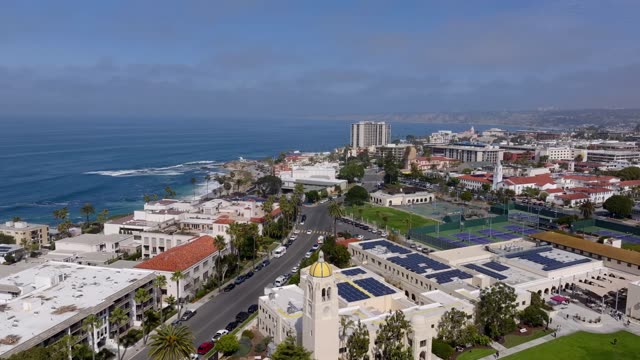 Aerial footage over the Village of La Jolla with tennis courts, rooftops and coastline in view | Drone Video