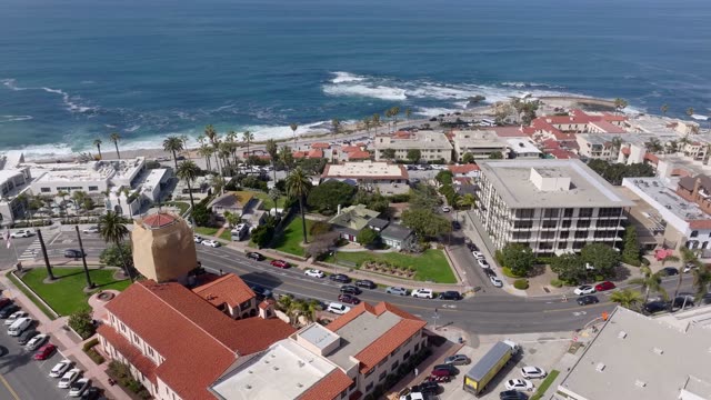 Aerial footage over the Village of La Jolla showing rooftops, palm trees and the coastline | Drone Video