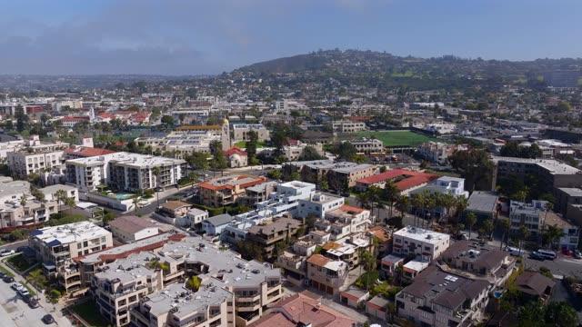 Aerial footage over the Village of La Jolla showing rooftops, church steeples and Mount Soledad beyond | Drone Video