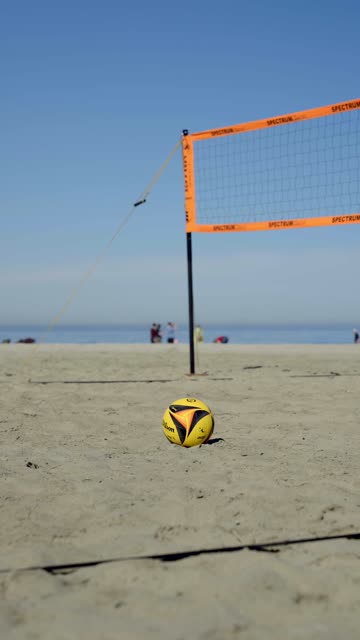 Volleyball and net set up on the sand with the ocean in the background at Moonlight Beach in Encinitas coastline | Vertical Video