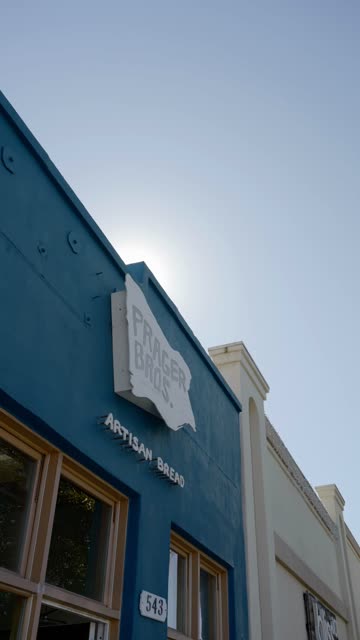 Prager Bros. Artisan Bread sign on a blue storefront with sun flare in the sky above downtown Encinitas | Vertical Video