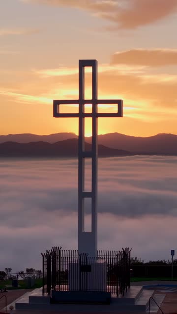 Aerial footage of the Mount Soledad Veterans Memorial cross rising above a layer of clouds at sunrise in La Jolla | Vertical Drone Video