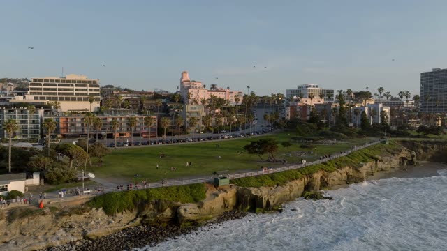 Aerial footage of the La Valencia Hotel and Ellen Browning Scripps Park with palm trees and coastline near La Jolla Cove | Drone Video