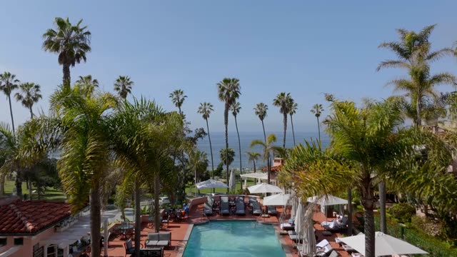 Aerial drone footage flying over La Valencia Hotel pool and palm trees toward Scripps Park and open ocean near La Jolla Cove | Drone Video