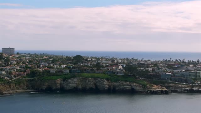 Aerial footage of kayakers paddling near sandstone sea caves below the village and cliffs of La Jolla Cove in La Jolla | Drone Video
