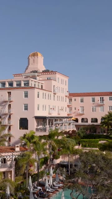 Aerial footage of the La Valencia Hotel also known as the Pink Lady with its dome, pool and palm trees above La Jolla Cove in La Jolla | Vertical Drone Video