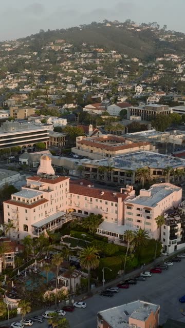 Aerial footage of the pink La Valencia Hotel, palm trees and hillside homes above La Jolla Cove in La Jolla | Vertical Drone Video