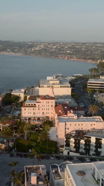 Aerial footage of the La Valencia Hotel pink facade with the La Jolla coastline, village streets and palm trees stretching toward Scripps Pier | Vertical Drone Video