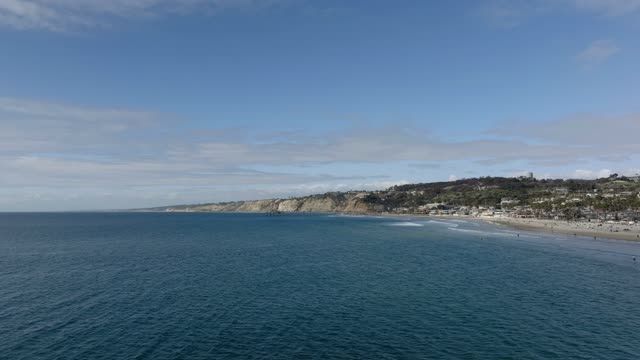 Aerial footage flying over open water toward La Jolla Shores beach, coastal cliffs and hillside neighborhoods above La Jolla | Drone Video
